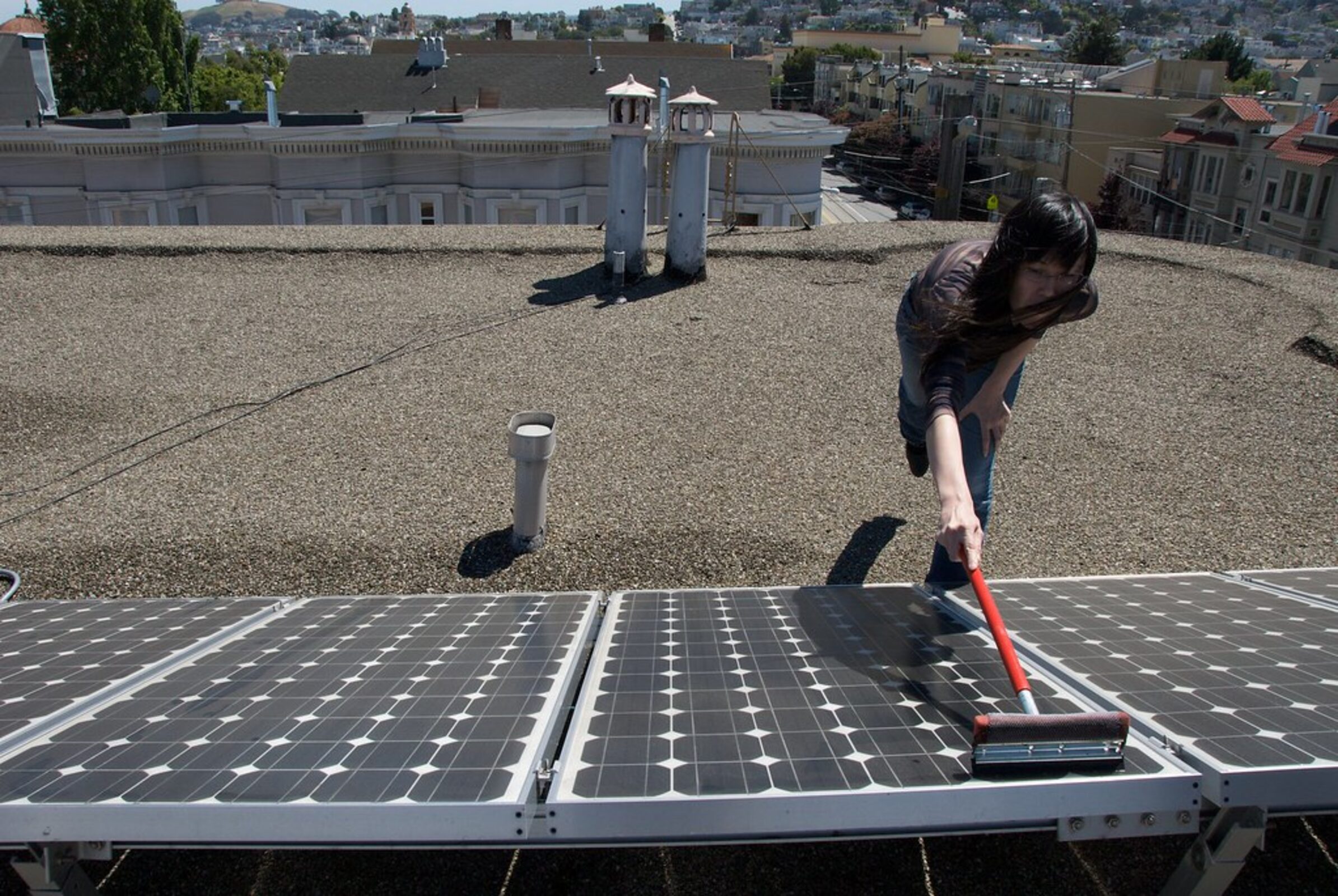 Technician cleaning rooftop solar panels in California sunlight